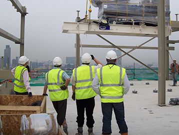 Men on building site providing project management expertise whilst watching a generator set being lifted by crane