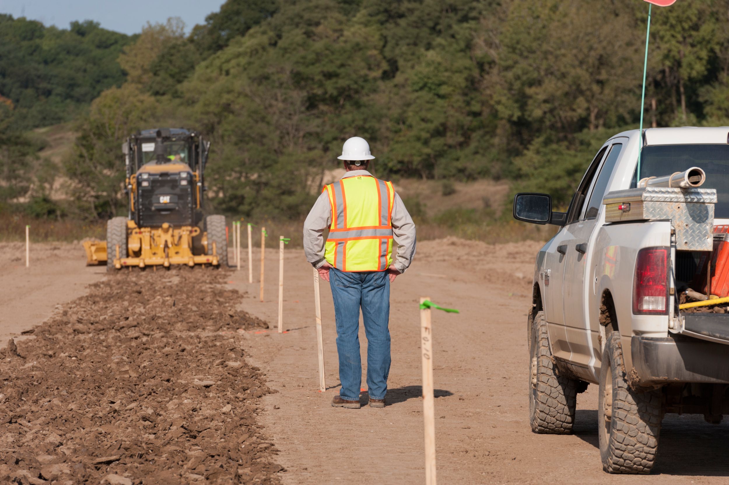 A motor grader scarifies the existing ground to prepare for compaction and fill. Without AccuGrade™ technology, between 250-300 stakes have to be set per mile for a typical four-lane highway.