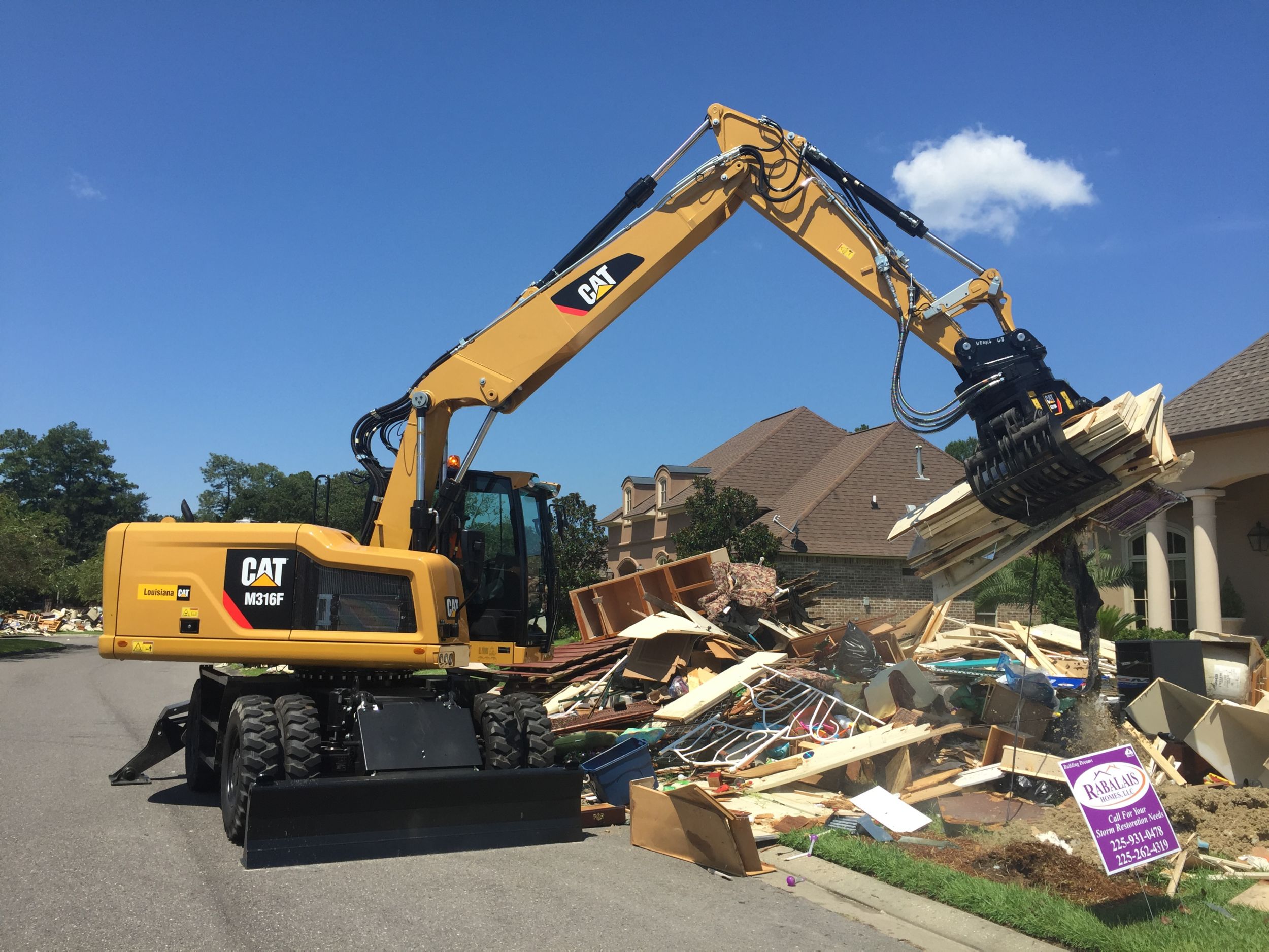 A Cat® M316F Wheeled Excavator picks up debris in a residential neighborhood affected by the historic floods in southern Louisiana.