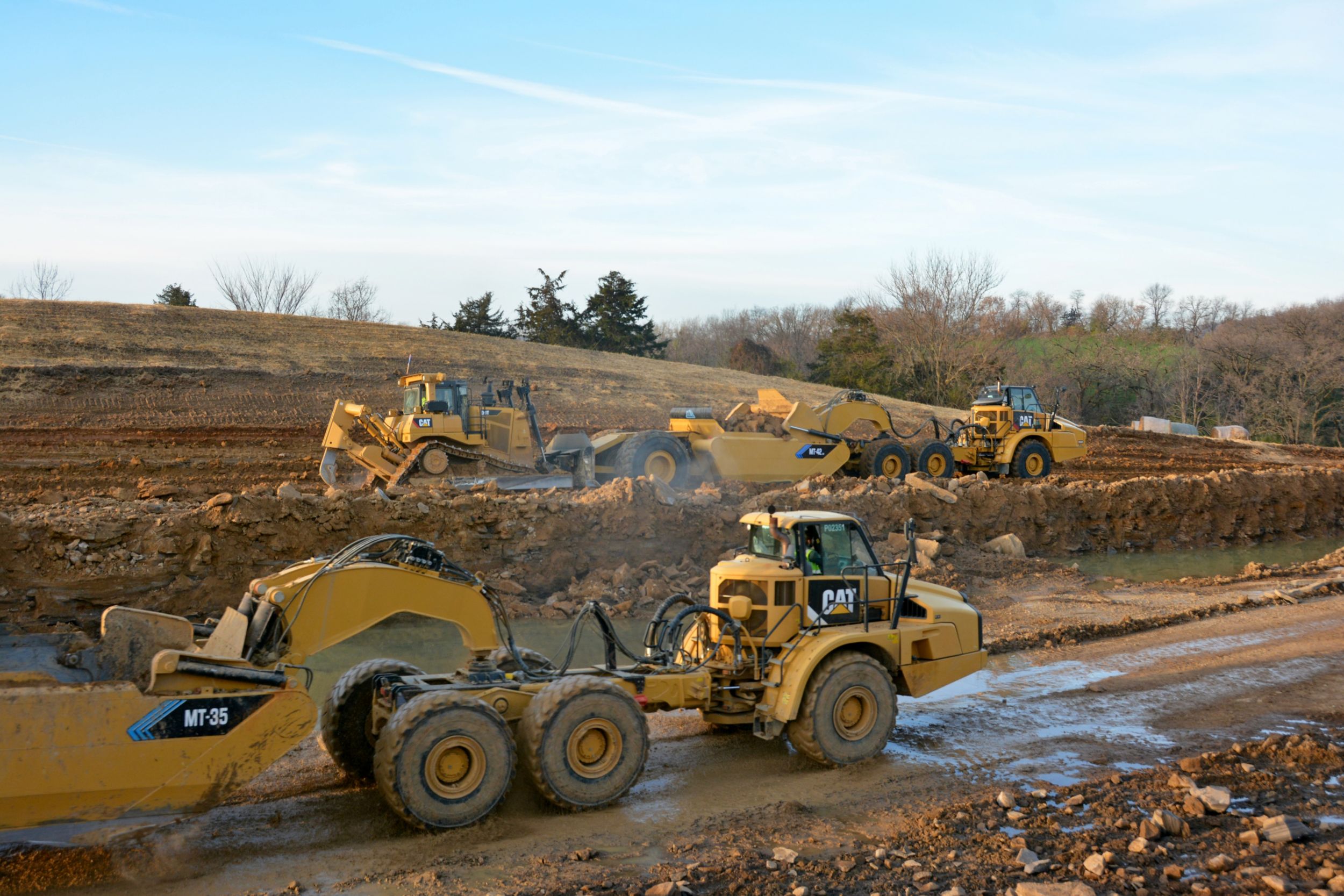 A Cat® 745 Articulated Truck chassis is converted from a dump body configuration to a scraper power unit. The scrapers are being push loaded by a pair of Cat D9T Dozers and a Cat D8T Dozer.