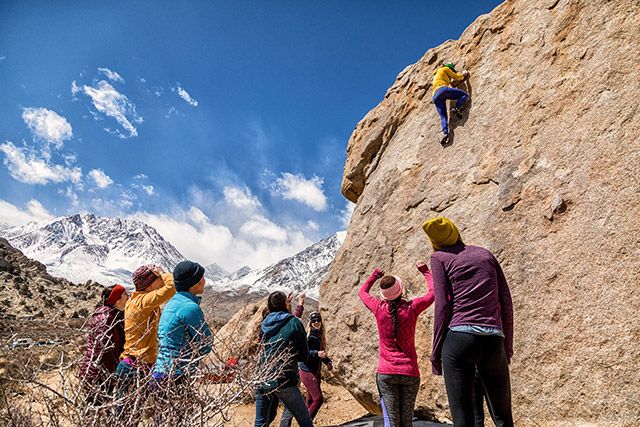 A group of people watch as a climber maneuvers up a boulder.