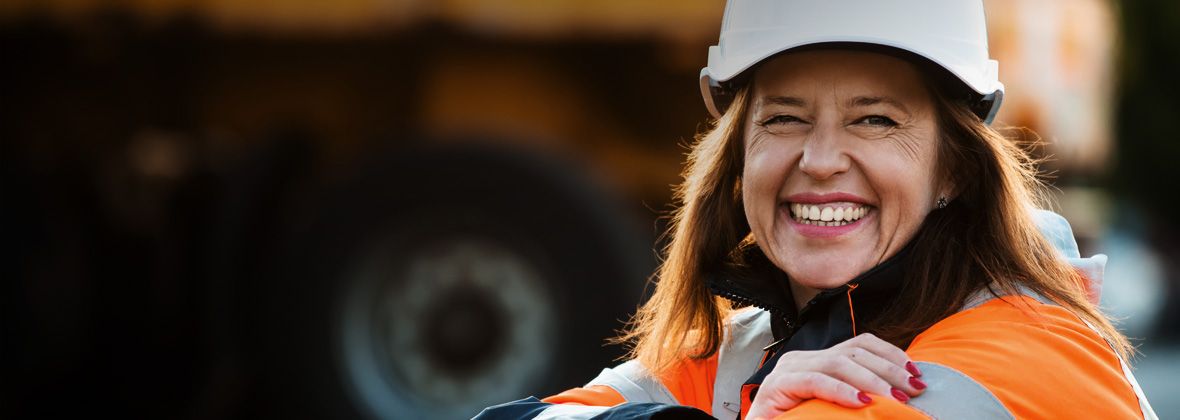 Un travailleur isolé sourit à la caméra, portant un casque de sécurité et une veste résistante