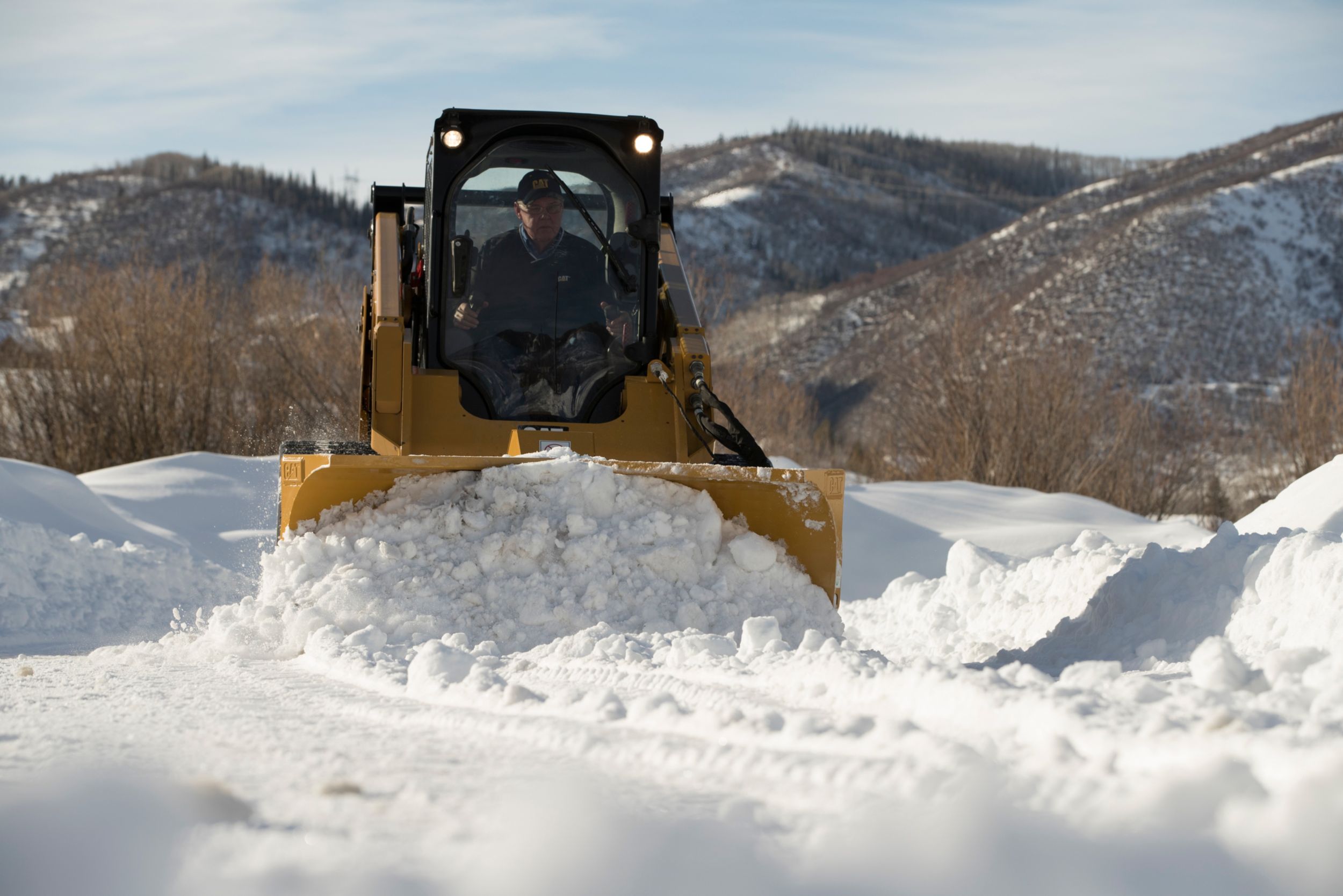 Chasse-neige en V multifonction Cat poussant la neige en configuration godet