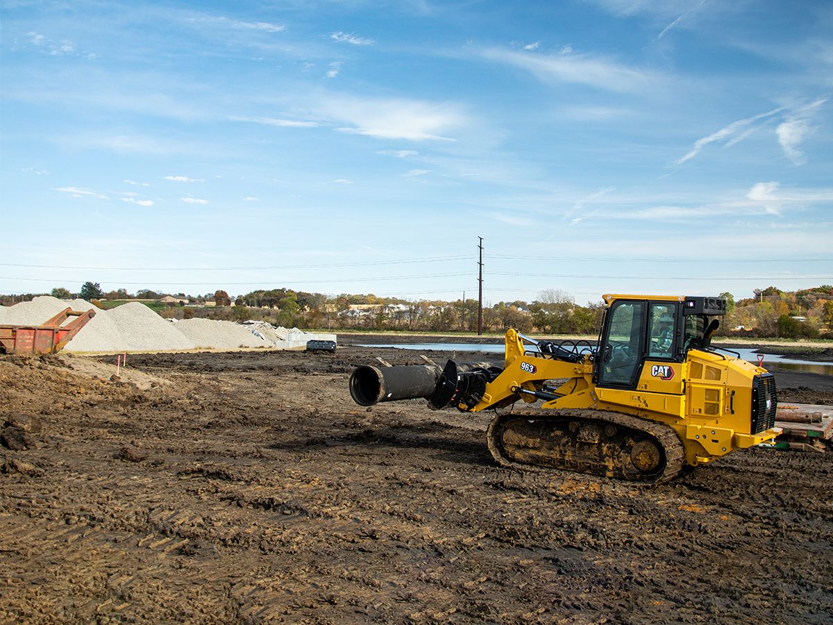 Chargeuse à chaînes 963 Cat transportant une canalisation sur des travaux de voirie