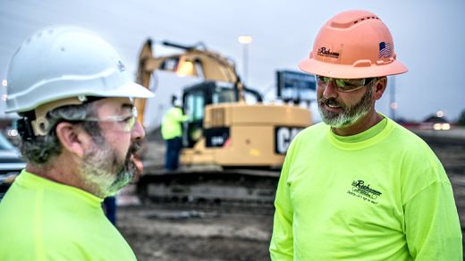 Male customer using Ipad with Excavator working in the background