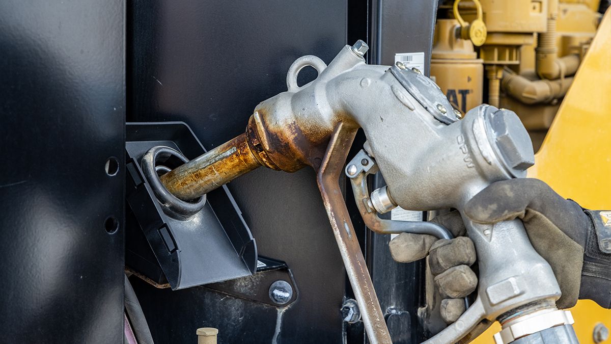 Industrial sized fuel nozzle being lifted by gloved hand out of petrol pump