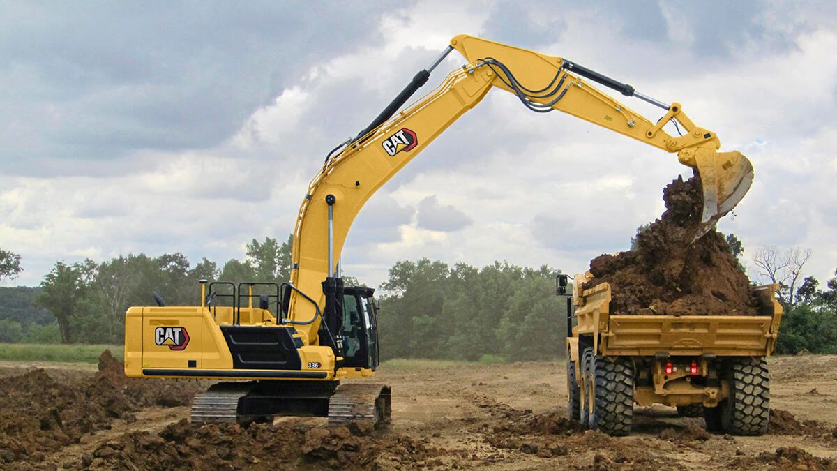 Excavator in a field, loading dirt into truck alongside
