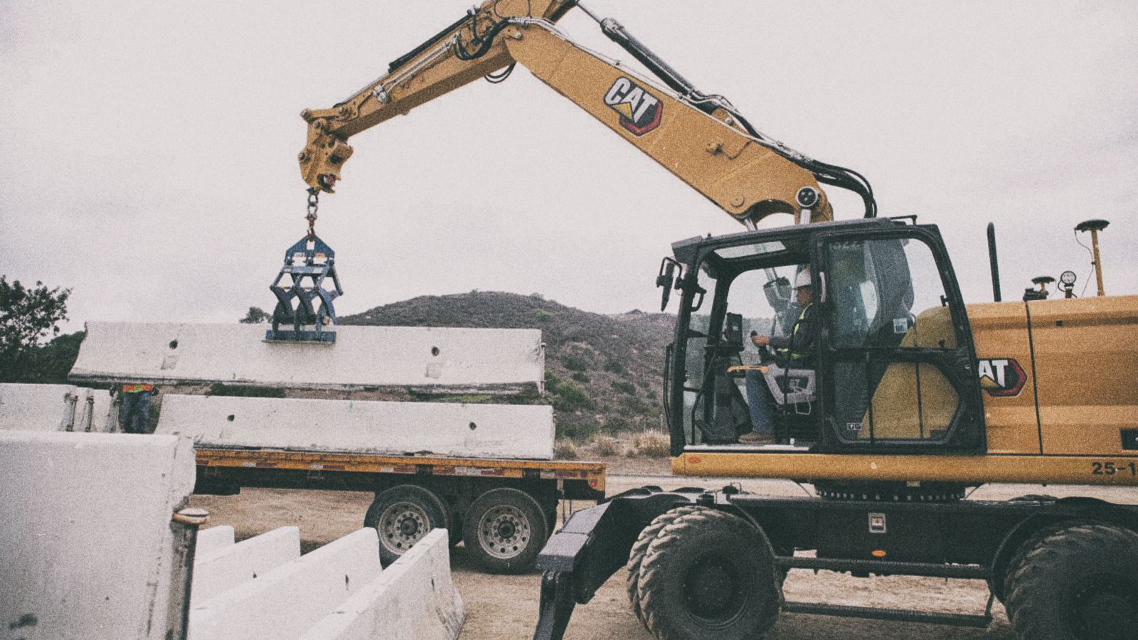M322 Excavator lifting concrete dividers on jobsite