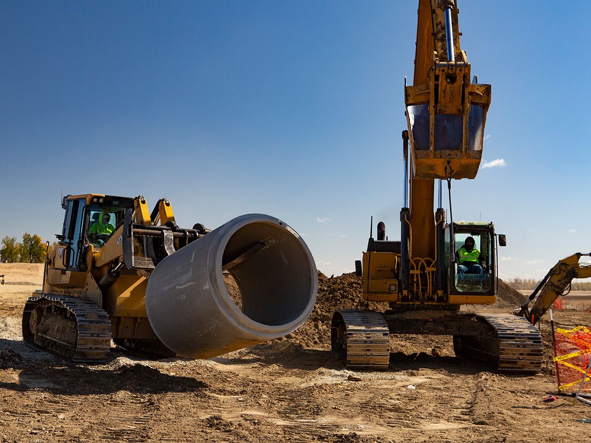 De 973-rupslader doet het zware werk voor de installatie van rioolbuizen