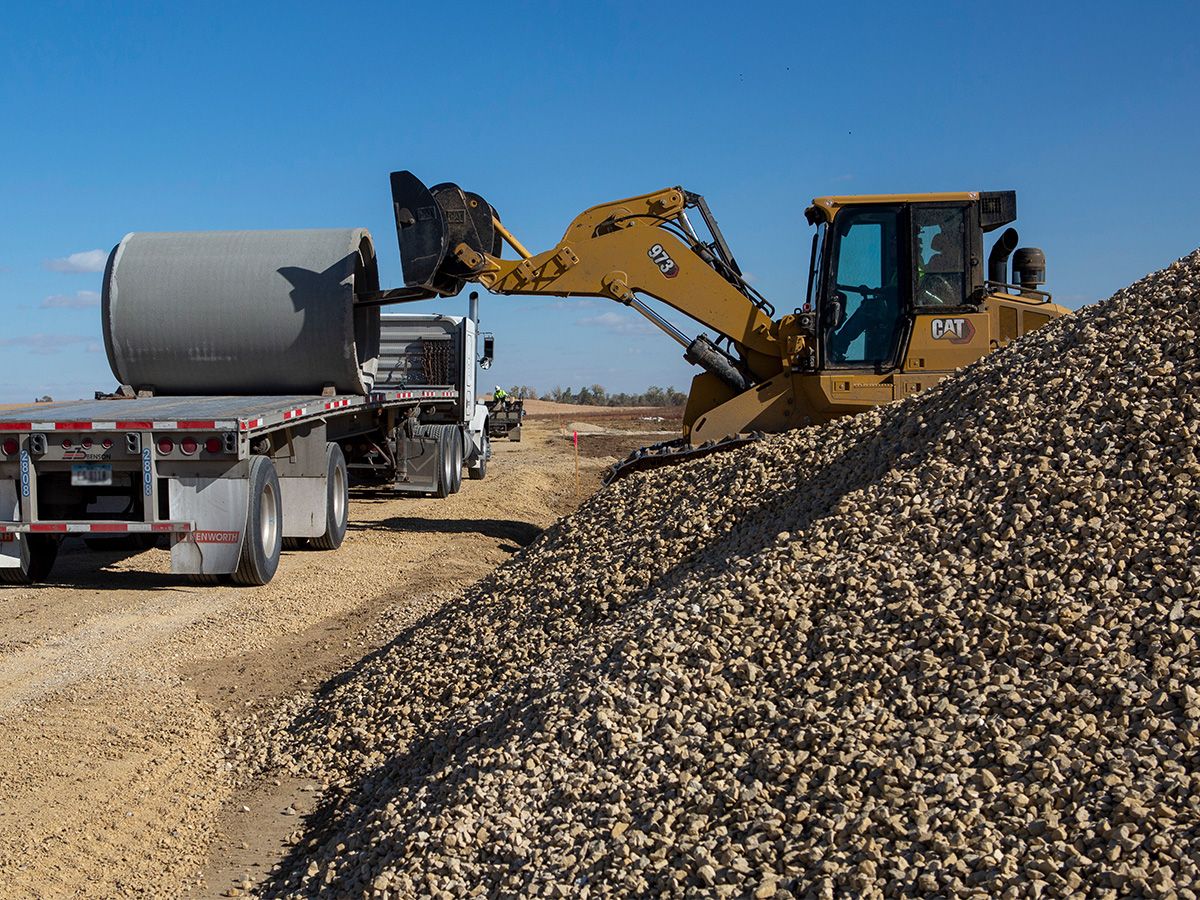 Ładowarka gąsienicowa 973 z widłami rozładowująca kręgi betonowe