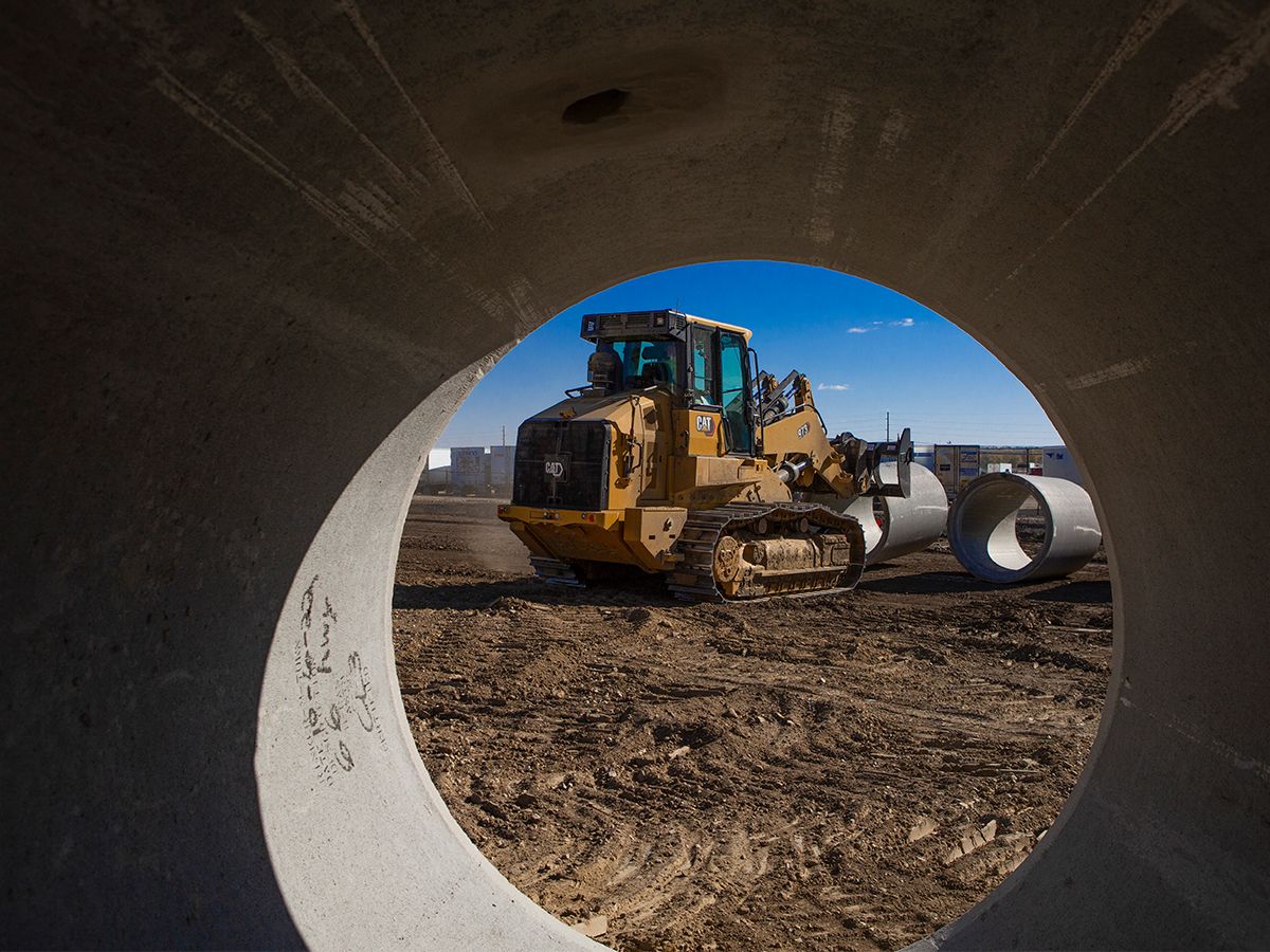 973 crawler loader with a quick coupler picking up sewer pipe, as seen through a concrete pipe