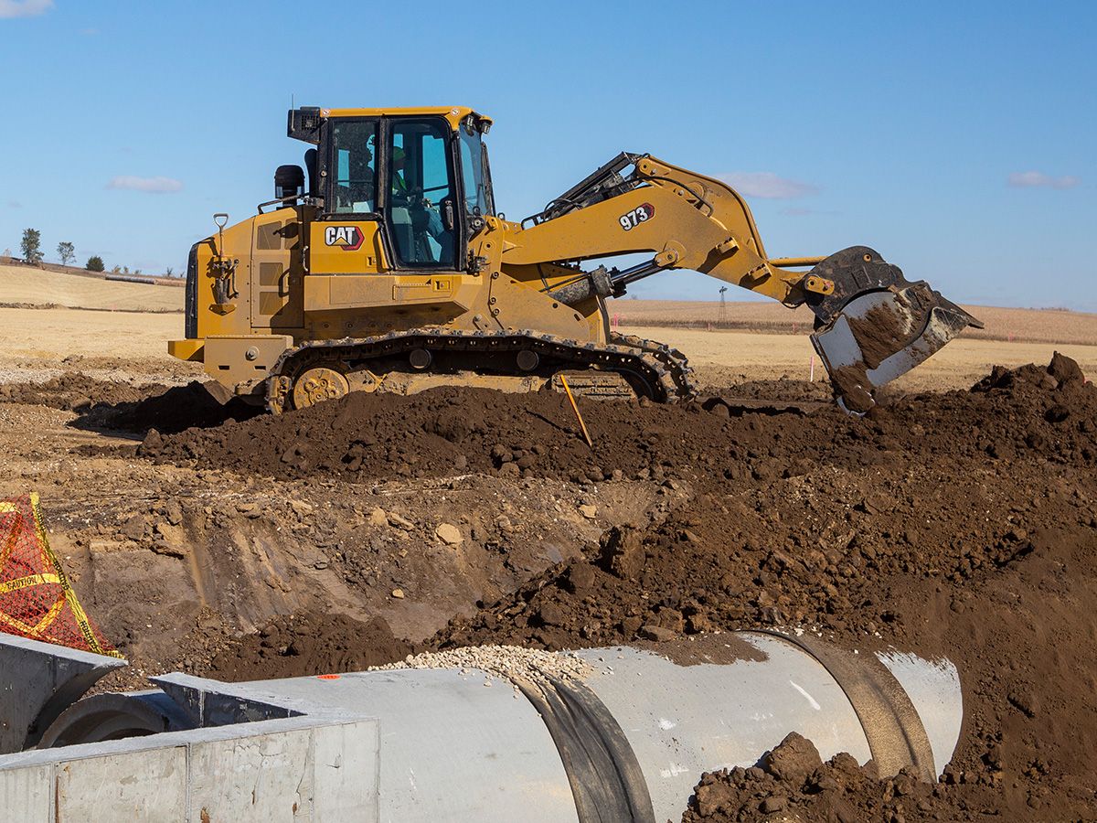 Chargeuse à chaînes 973 en plein travail avec des pelles hydrauliques sur un projet d'installation d'égouts