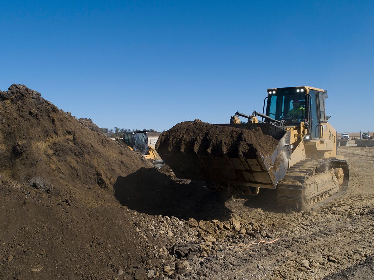 A 973 crawler loader with a bucket carries fill dirt on the job site