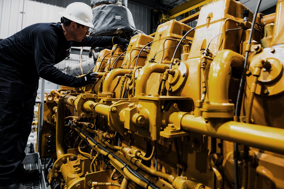 Close up of Cat worker in PPE leaning over to work on a Cat G3600 A4 Gen 2 Engine