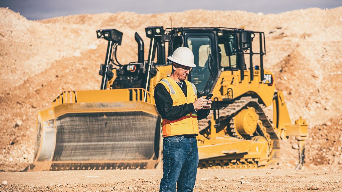 Person utilizing a cellular device with a tractor in the background - Improve Fleet Utilization