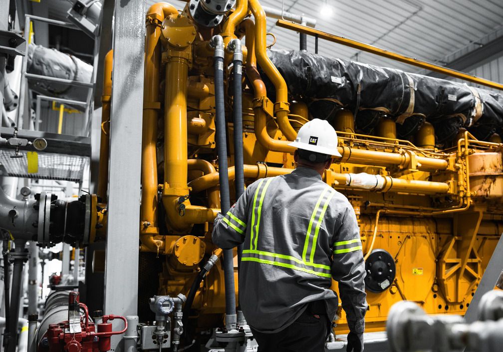 Cat worker in PPE with his back to the camera staring at Cat G3600 Engine