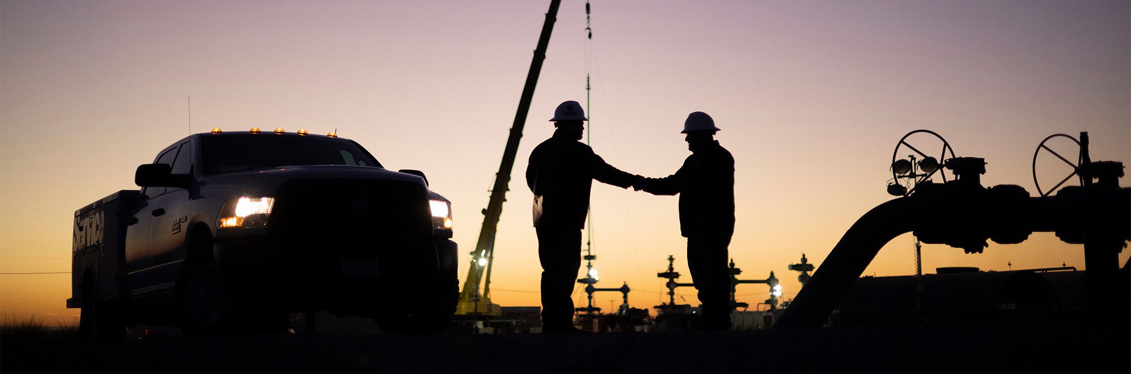 Two men in PPE standing and shaking hands on a jobsite at sunset