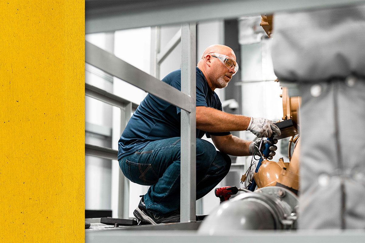 Close up of Cat worker kneeling down next to Cat engine while looking at data