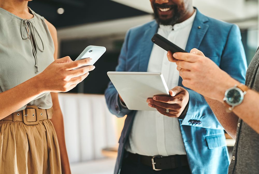 Three people looking at phones and tablets.