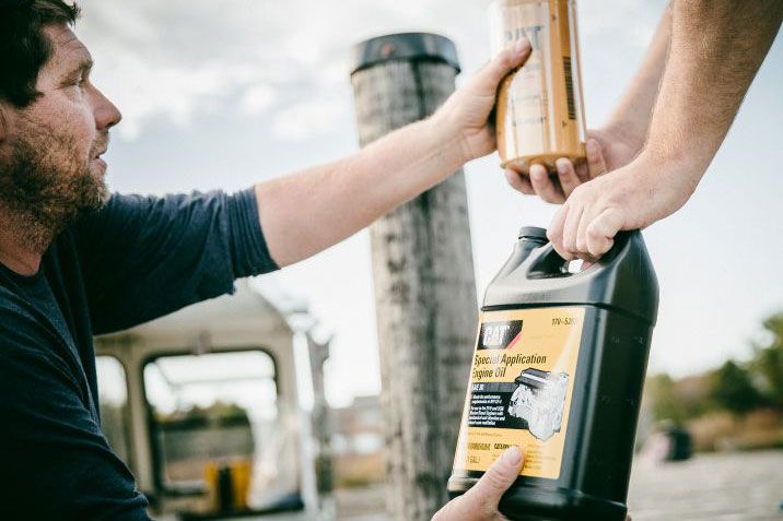 Person handing Cat filter and oil container to someone standing on a boat dock