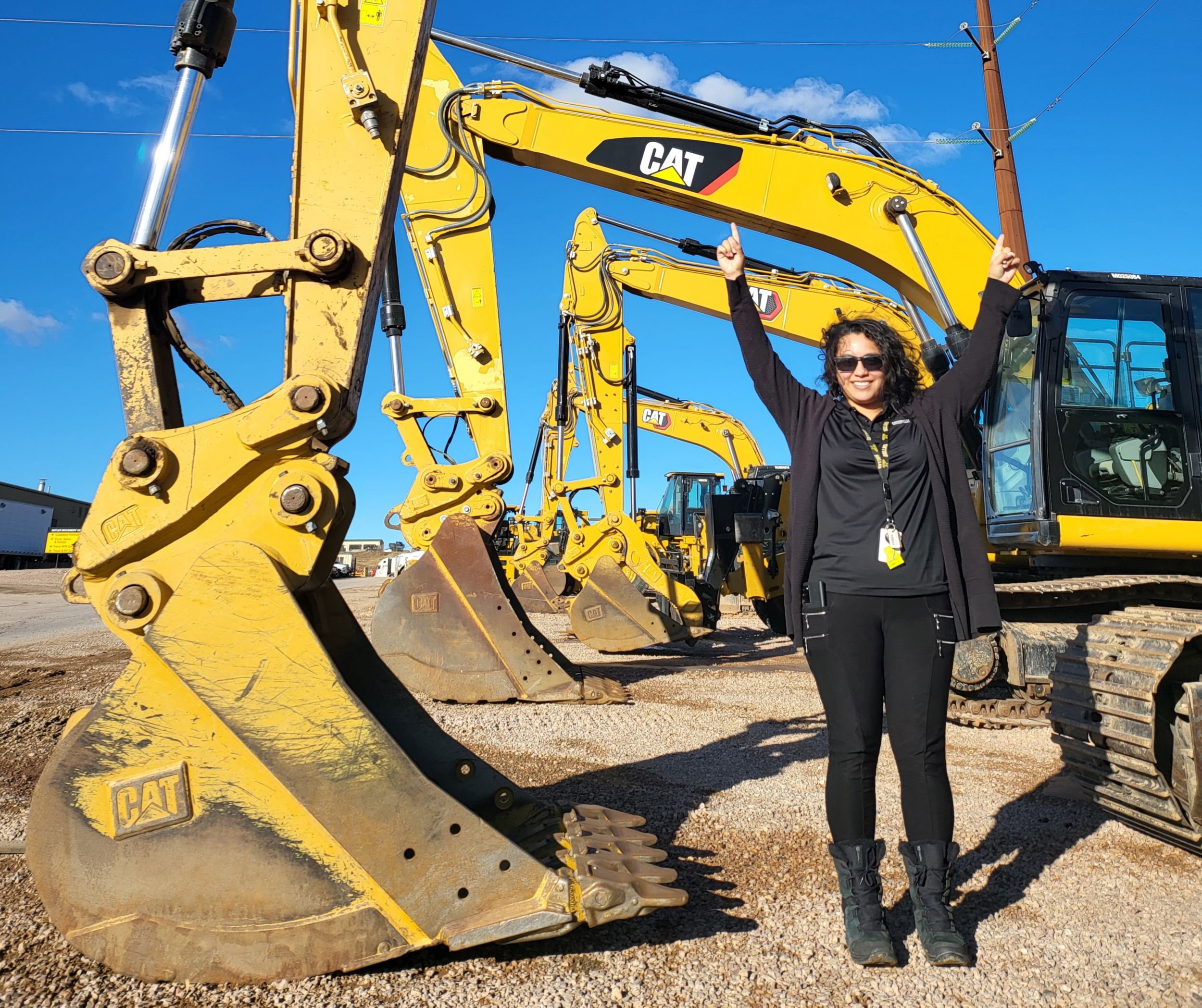 Cesia Viera standing in front of a lineup of excavators, pointing at the boom
