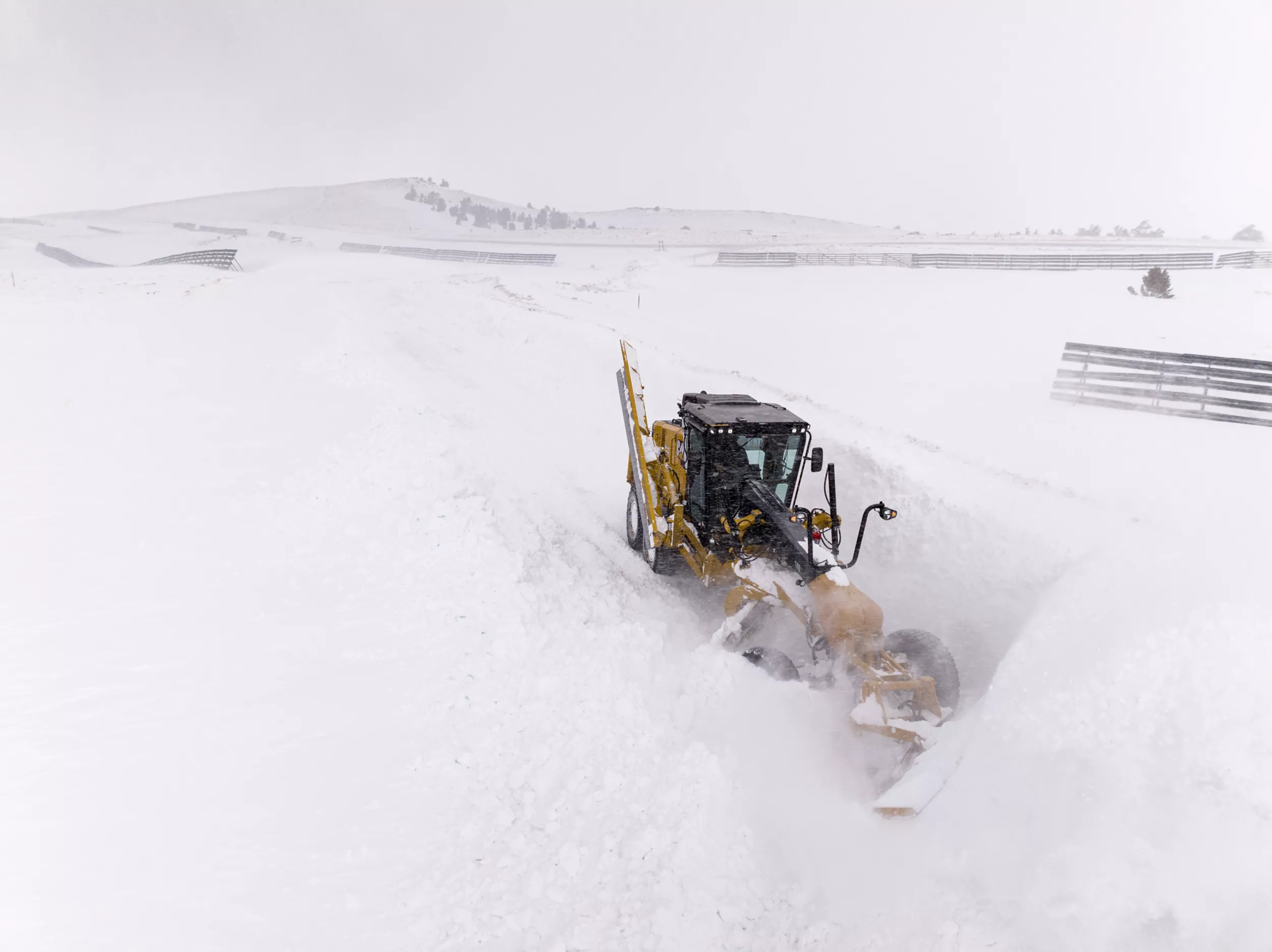140 Motor Grader pushing snow in six-foot high snowdrifts. The machine has a snow wing in the upright position and a v-plow at the front moving the snow.