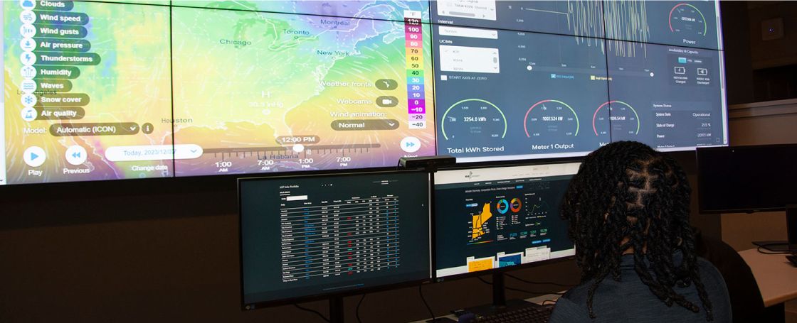 Employee working at a computer in front of monitors of a weather map and usage meters