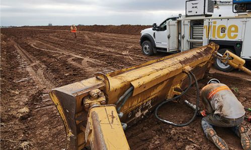 A service technician works on a dozer blade in front of a service truck