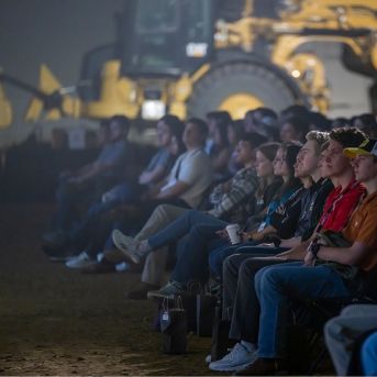 Interns sit to watch an orientation presentation in an arena in front of Cat equipment