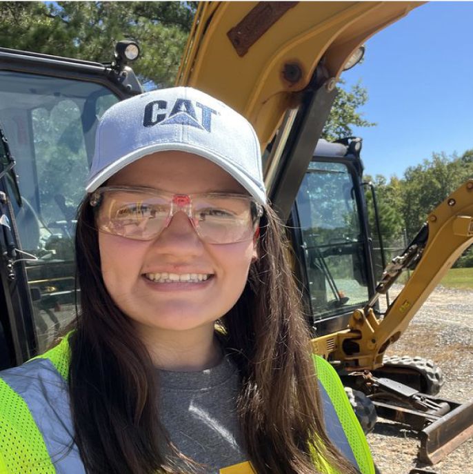 A woman stands in front of Cat mini excavators