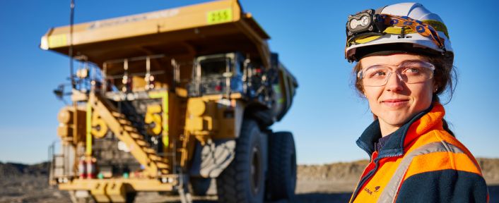Woman in a hard hat and orange jacket standing in front of a Cat mining truck