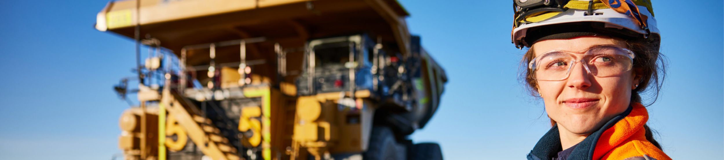 Woman wearing safety glasses and a hardhat standing in front of a Cat mining truck