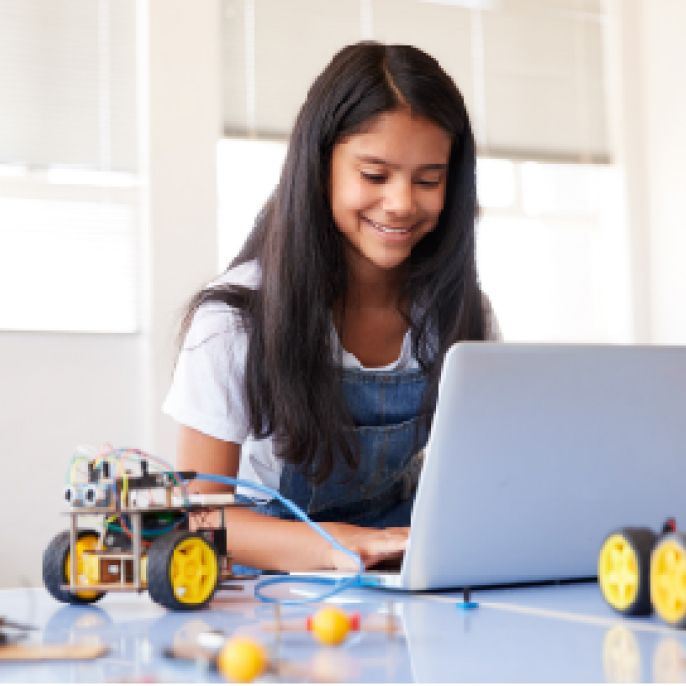 A girl works on a computer while building a robot