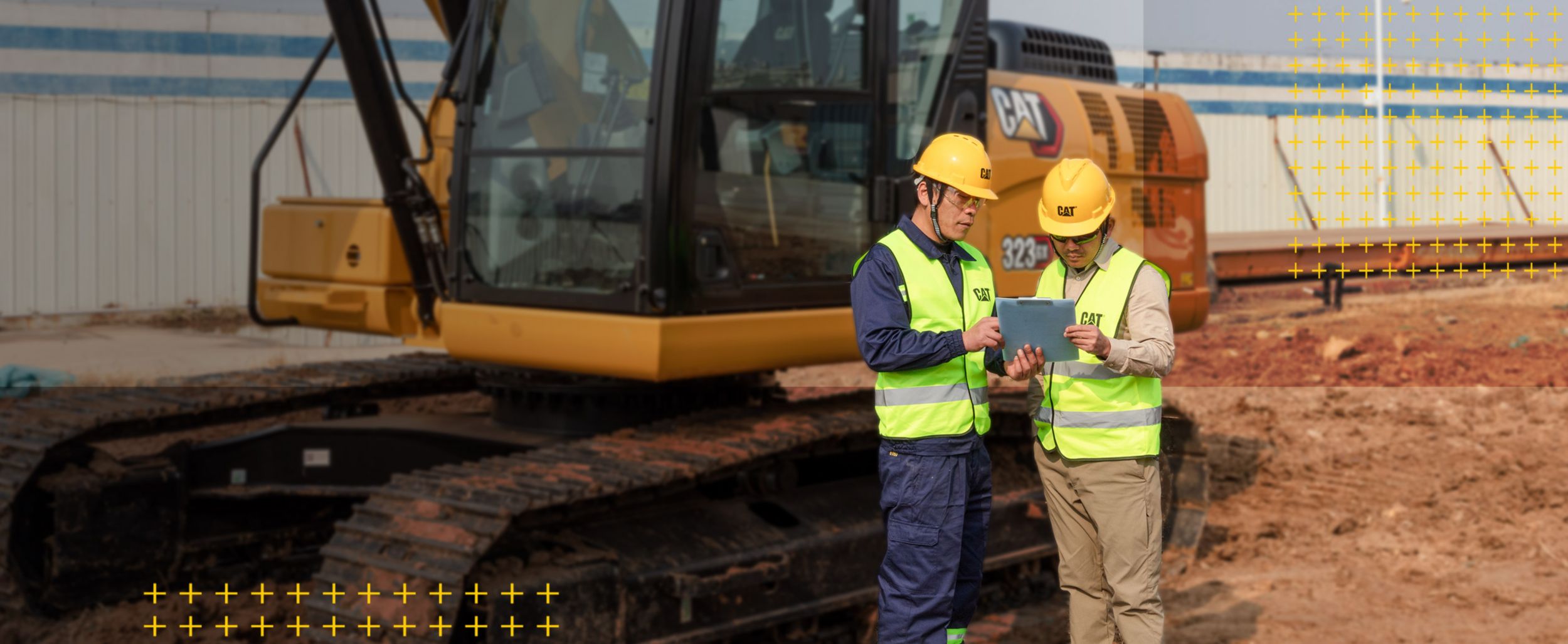 Two workers looking at clipboard in front of excavator