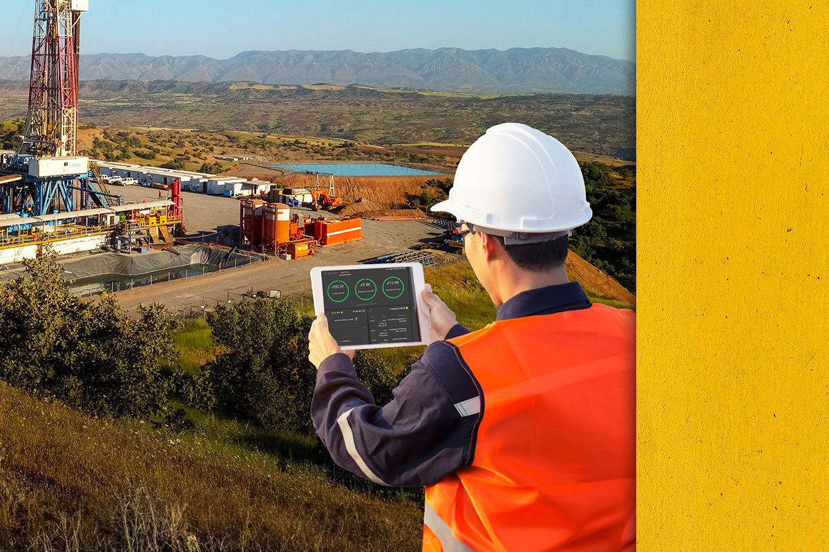 Back view of a Cat worker in PPE looking at Data on an iPad with a jobsite in the distance