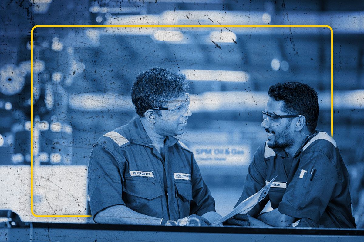 Two SPM Cat workers dressed in PPE having a conversation against a blurred background shaded in blue