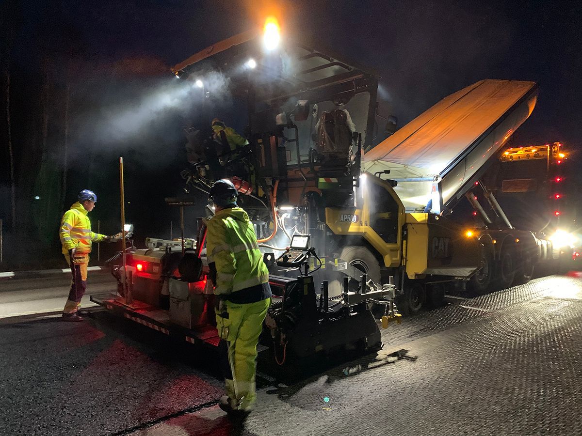 Ein Straßenbauteam arbeitet nachts mit dem Asphaltfertiger AP500.
