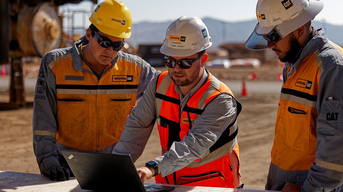 three workers at site looking at computer together
