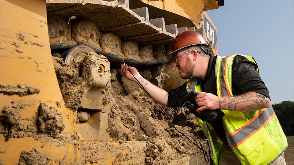 Man inspecting undercarriage of Cat Machine