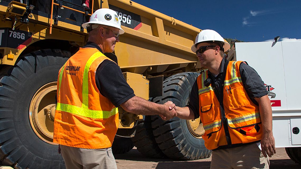 Dos personas se dan la mano cerca de un camión para la minería de Cat