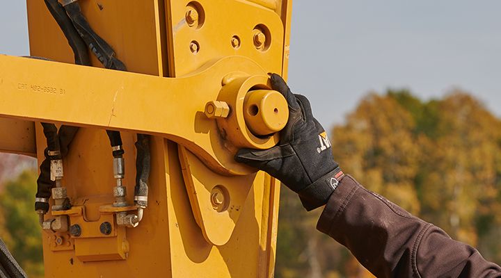 Hand wearing a Cat glove, touching the end of a linkage pin on an excavator stick