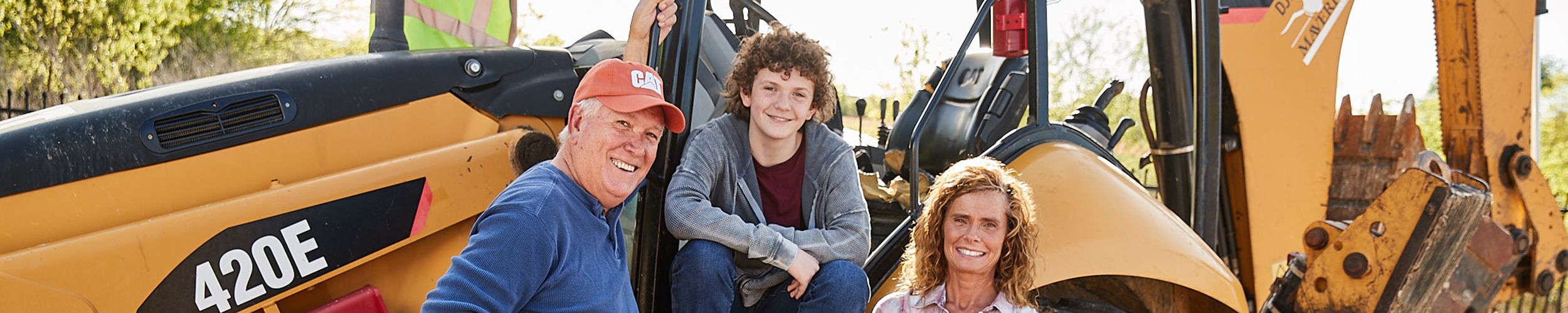 A male Caterpillar retiree stands with family in front of a 420E backhoe.
