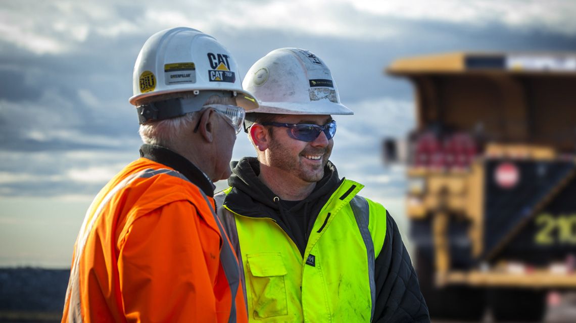 Two men wearing hard hats, one smiling