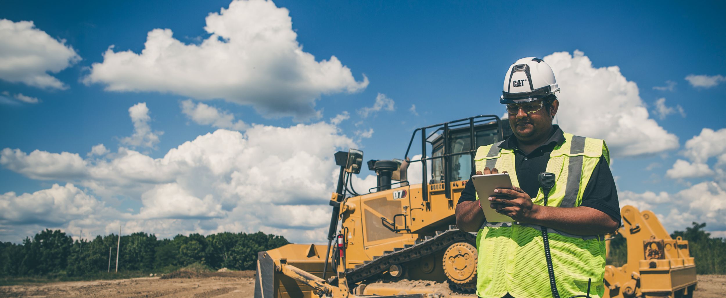 worker using assistance technology on a tablet with a D7 Dozer in the background of a jobsite