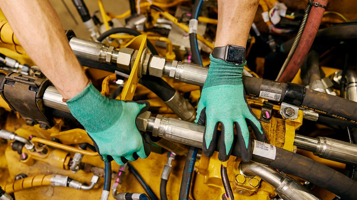 Manos con guantes agarrando piezas de mangueras en un motor Cat