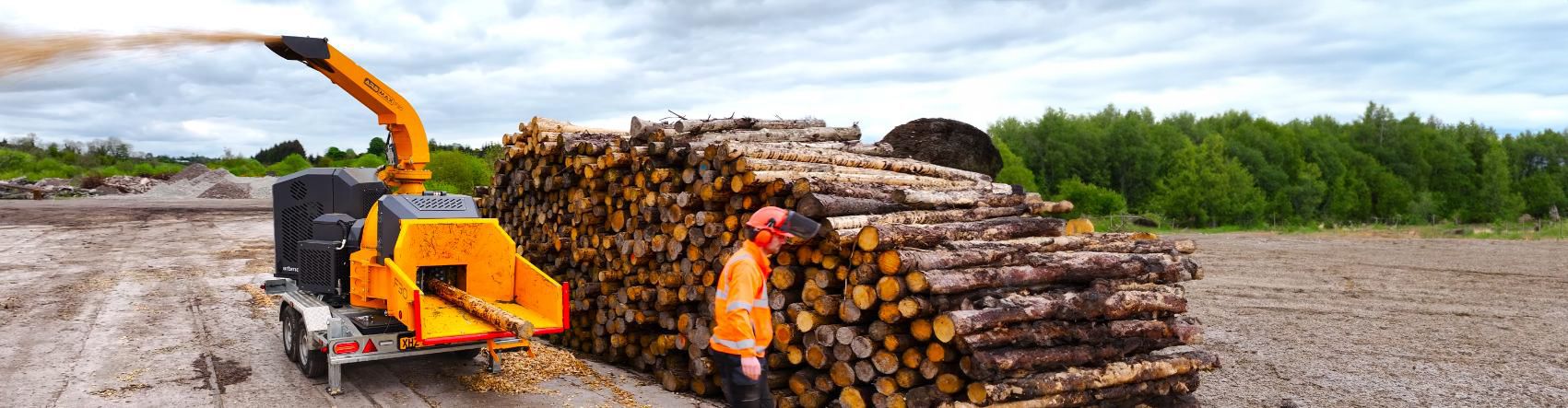 ARBMAX wood chipper processing wood next to machine operator wearing personal protective clothing.
