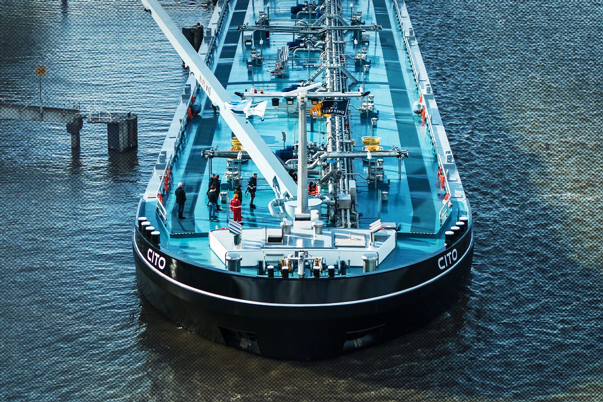 The prow of a large maritime vessel making its way through the gray waters of an inland waterway.