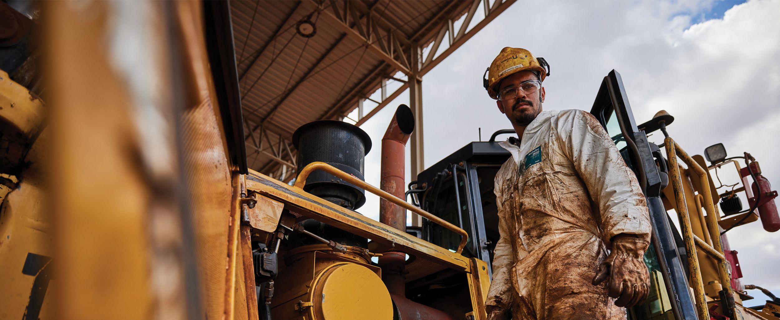 Man covered in dirt standing on Cat mining machine with cabin door ajar