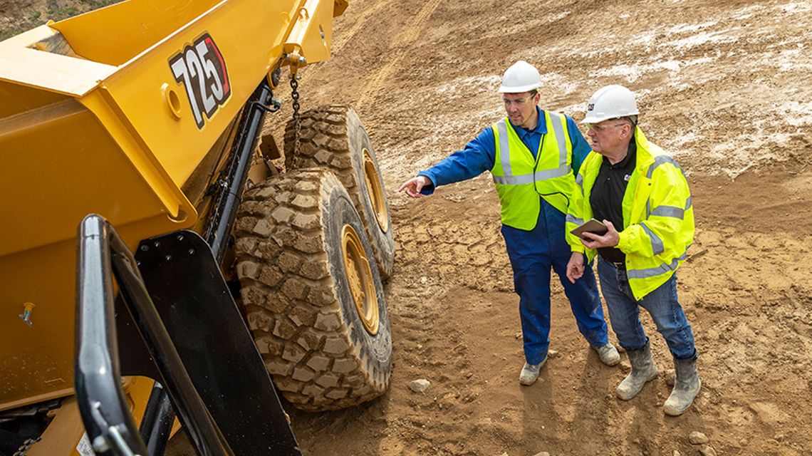 Two men looking a Cat mining articulated truck