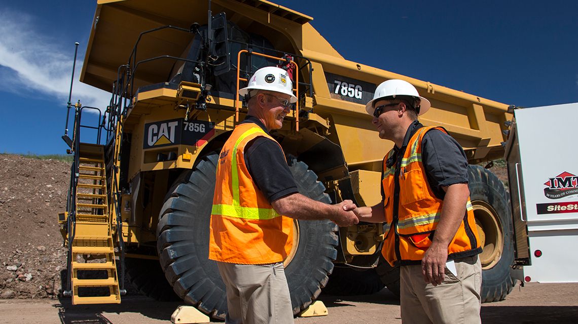 Two men shaking hands near Cat mining truck